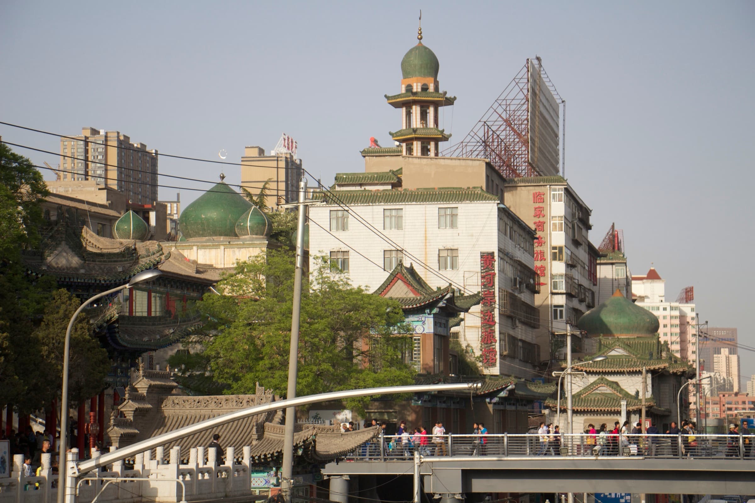 Dans une périphérie en travaux, une mosquée à coupole verte et minaret voisine avec un immeuble sous échafaudage et une tour à toits de pagode.