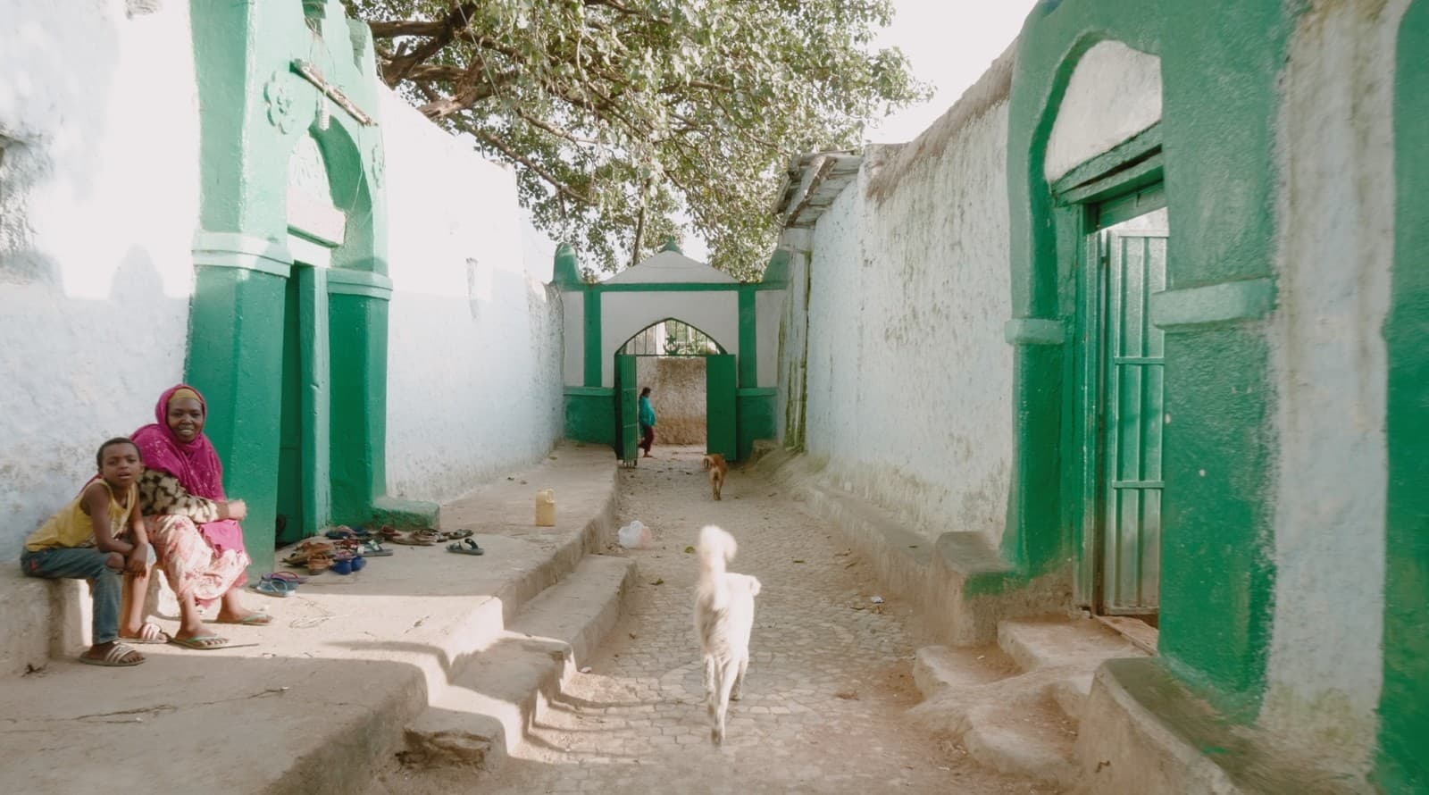 Une mère et son enfant dans une ruelle aux murs blancs et verts de Harar